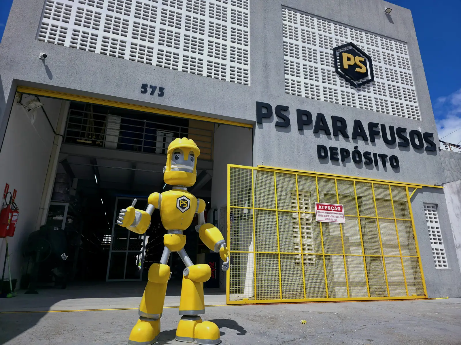 Fachada do depósito da PS Parafusos, com o mascote na frente e o portão de recebimento de mercadoria